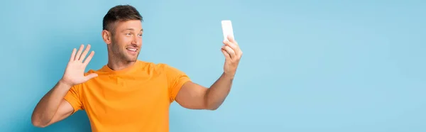 Мужчина в футболке держит смартфон и делает селфи, размахивая рукой на синем баннере — стоковое фото