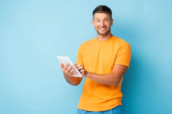 Homme heureux en t-shirt tenant tablette numérique sur bleu — Photo de stock