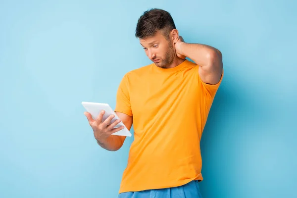 Confused man in t-shirt using digital tablet on blue — Stock Photo