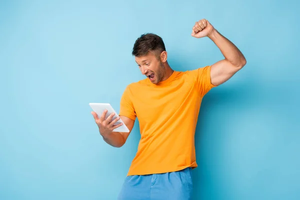 Homme excité avec poing serré en utilisant une tablette numérique sur bleu — Photo de stock