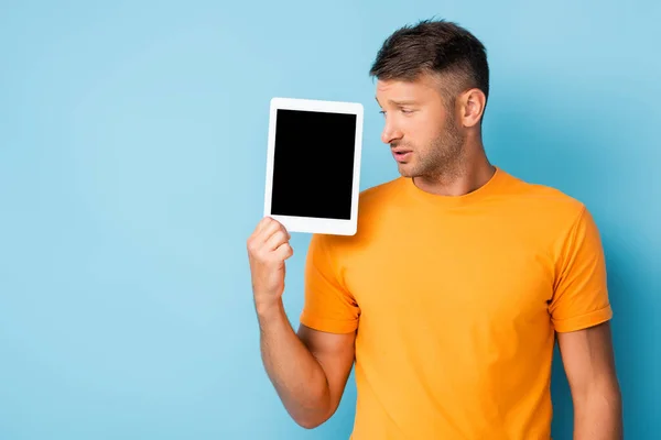 Mann im T-Shirt hält digitales Tablet mit leerem Bildschirm auf blau — Stockfoto