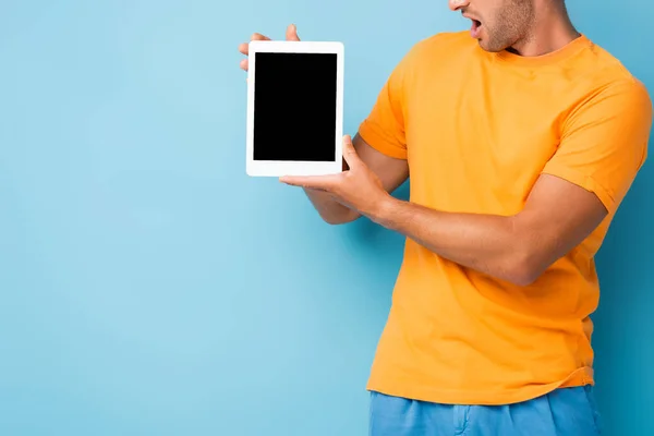 Vista recortada del hombre sorprendido en camiseta sosteniendo tableta digital con pantalla en blanco en azul - foto de stock