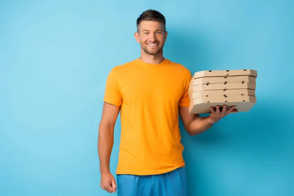 Hombre feliz sosteniendo cajas de pizza de cartón en azul - foto de stock