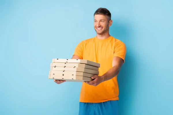 Cheerful man in t-shirt holding carton pizza boxes on blue — Stock Photo