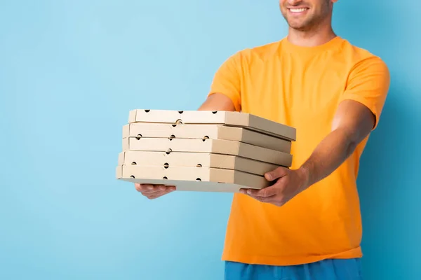 Vue recadrée de l'homme heureux en t-shirt tenant boîtes à pizza carton sur bleu — Photo de stock