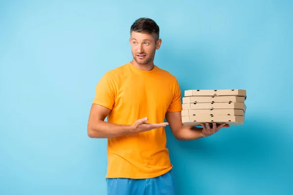 Mann im T-Shirt zeigt mit der Hand auf Pizzakartons auf blauem Grund — Stockfoto