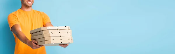 Vue recadrée de l'homme heureux en t-shirt tenant boîtes à pizza carton sur bleu, bannière — Photo de stock
