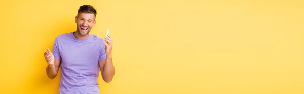 Hombre emocionado sosteniendo el teléfono inteligente y riendo en amarillo, bandera - foto de stock