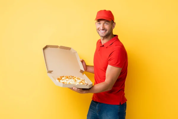 Heureux livreur dans la boîte de maintien chapeau rouge avec pizza savoureuse sur jaune — Photo de stock