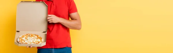 Vista ritagliata del fattorino che tiene la scatola con gustosa pizza sul giallo, banner — Foto stock