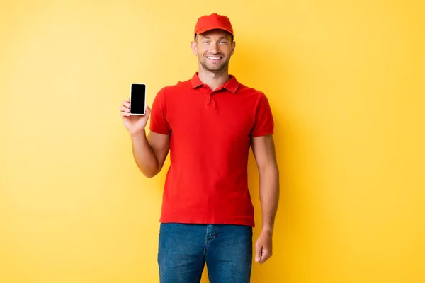 Repartidor en tapa roja sosteniendo smartphone con pantalla en blanco en amarillo - foto de stock