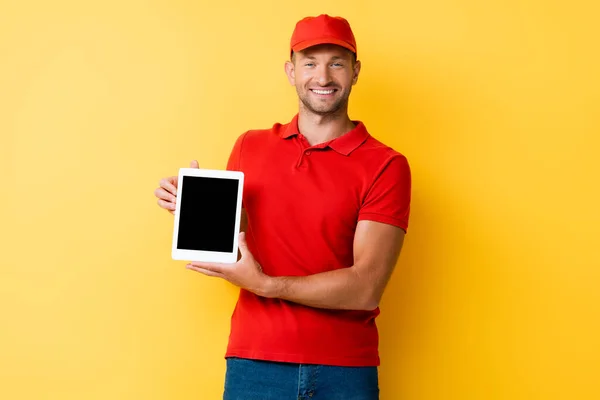 Felice uomo di consegna in tappo rosso con tablet digitale con schermo bianco su giallo — Foto stock