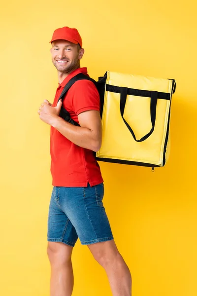 Cheerful delivery man carrying backpack with order on yellow — Stock Photo