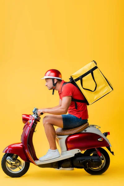 Вид збоку на людину доставки з рюкзаком їзда скутер на жовтому — стокове фото
