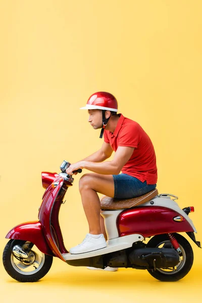 Вид збоку концентрованого чоловіка в шоломі, що їде червоним скутером на жовтому — стокове фото