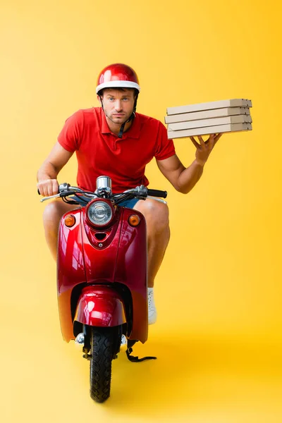 Fokussierter Zusteller mit Helm, der Roller fährt und Pizzakartons auf gelb hält — Stockfoto