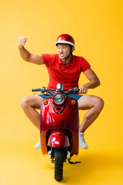 Роздратований чоловік в шоломі їде червоним скутером і показує згорнутий кулак на жовтому — стокове фото