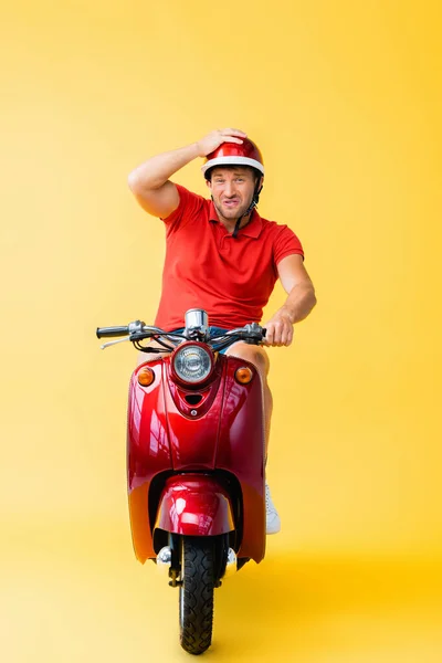 Незадоволений чоловік в шоломі їде червоним скутером і показує великий палець на жовтому — стокове фото