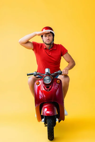 Hombre serio en casco a caballo scooter rojo y mirando lejos en amarillo - foto de stock