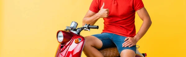 Cropped view of man sitting on red scooter and showing thumb up on yellow — Stock Photo