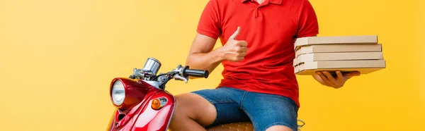 Cropped view of delivery man holding pizza boxes while showing thumb up near scooter on yellow — Stock Photo