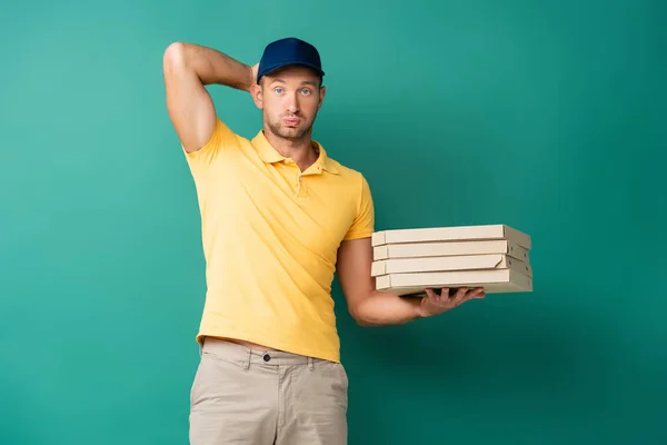 Uomo di consegna confuso in cap che tiene scatole di pizza sul blu — Foto stock