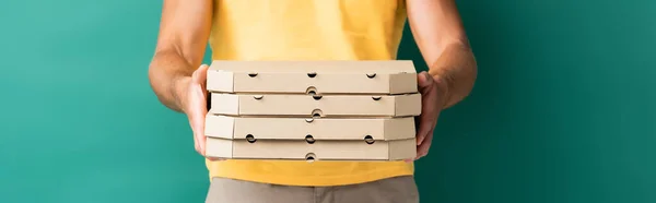 Vista recortada del repartidor con las manos extendidas sosteniendo cajas de pizza en azul, pancarta - foto de stock