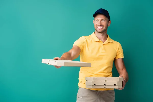 Homem de entrega alegre com mão estendida segurando caixas de pizza em azul — Fotografia de Stock