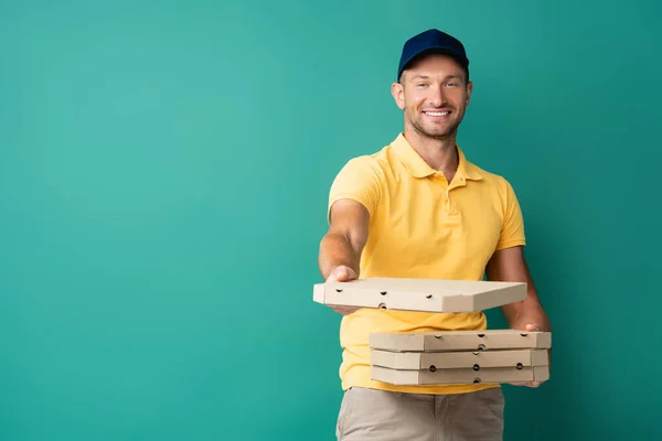 Livreur heureux avec main tendue tenant boîtes à pizza sur bleu — Photo de stock