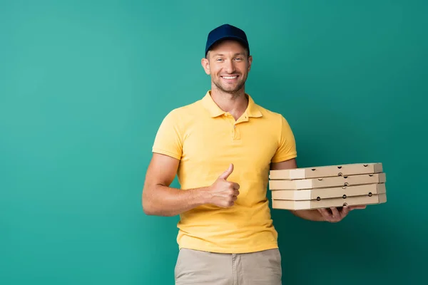 Glücklicher Lieferant hält Pizzakartons in der Hand und zeigt Daumen hoch auf blau — Stockfoto