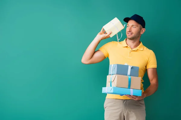 Чоловік доставки в уніформі і кепці тримає загорнуті подарунки на синьому — стокове фото