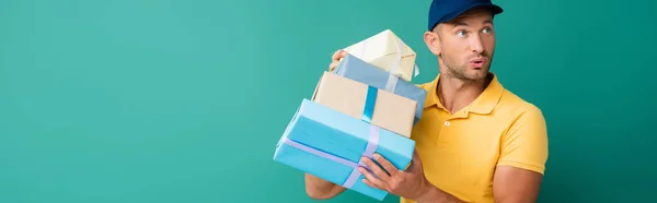 Homme de livraison curieux dans le capuchon tenant des cadeaux enveloppés sur bleu, bannière — Photo de stock