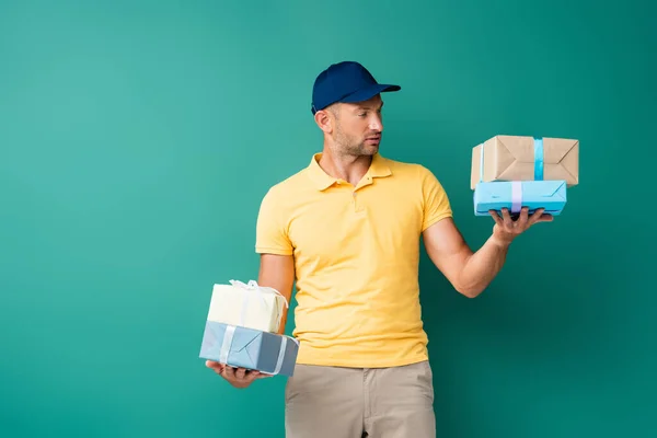 Delivery man in cap holding wrapped presents on blue — Stock Photo