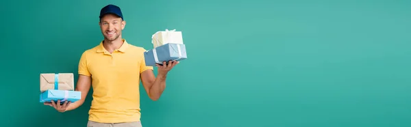 Glücklicher Auslieferer in Mütze mit verpackten Geschenken auf blauem Grund, Banner — Stockfoto