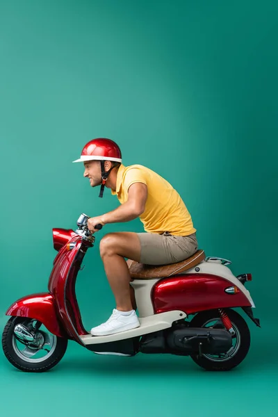 Profile of focused delivery man in helmet riding motorbike on blue — Stock Photo