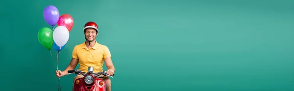 Homem de entrega feliz no capacete equitação scooter enquanto segurando balões em azul, banner — Fotografia de Stock