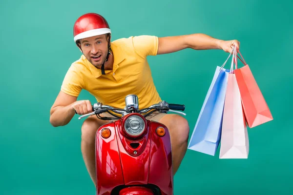 Liefermann mit Helm fährt Roller, während er Einkaufstüten auf blauem Grund hält — Stockfoto