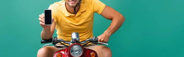 Vista cortada de homem de entrega feliz montando scooter enquanto segurando smartphone com tela em branco no azul — Fotografia de Stock