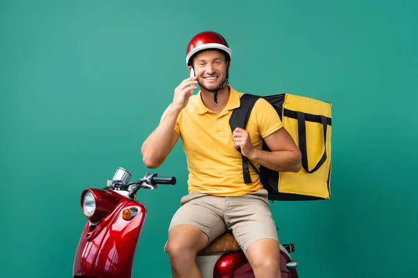 Allegro uomo di consegna con zaino parlare al telefono vicino scooter su blu — Foto stock
