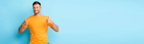 Happy man in yellow t-shirt showing thumbs up on blue, banner — Stock Photo