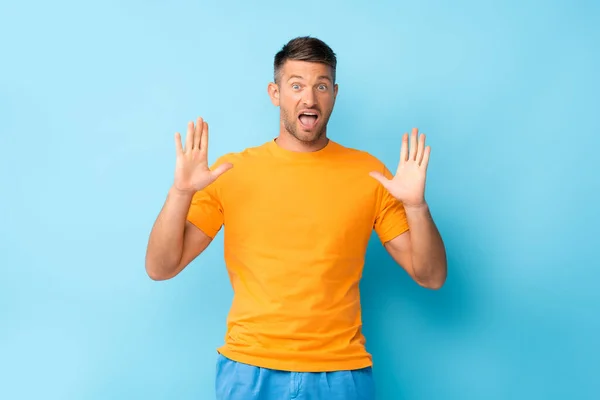 Shocked man in yellow t-shirt gesturing on blue — Stock Photo