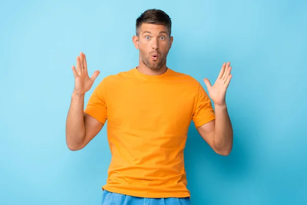 Surprised man in yellow t-shirt gesturing on blue — Stock Photo