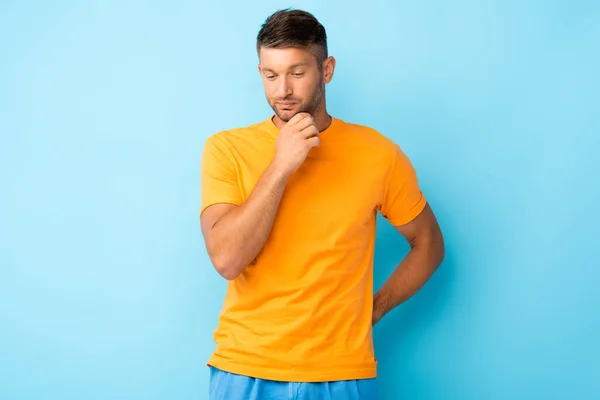 Homme réfléchi en t-shirt jaune regardant vers le bas sur le bleu — Photo de stock