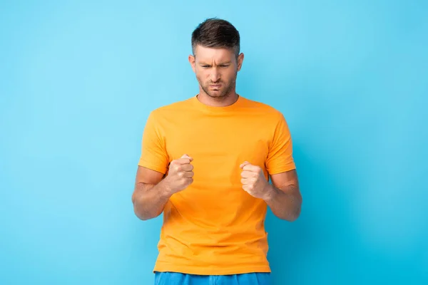 Homme irrité en t-shirt jaune debout avec des poings serrés sur bleu — Photo de stock