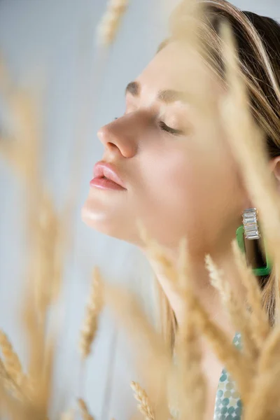 Jeune femme aux yeux fermés près des épillets de blé au premier plan flou — Photo de stock