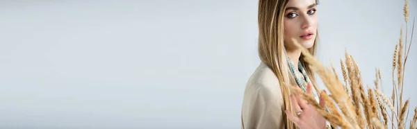 Woman looking at camera near wheat spikelets on blurred foreground, banner — Stock Photo