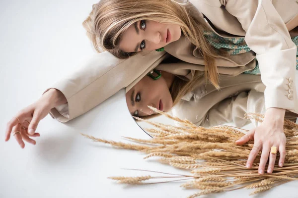 Junge Frau blickt in die Kamera in der Nähe von Weizenstacheln und Spiegel auf weiß — Stockfoto