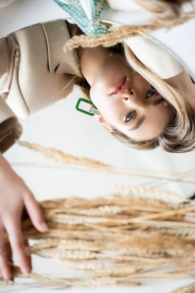 Vue du dessus de la jeune femme bouleversée regardant la caméra près des épillets d'orge sur blanc — Photo de stock