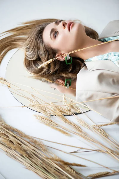 Giovane donna sdraiata vicino a grano e specchio mentre alza lo sguardo sul bianco — Foto stock