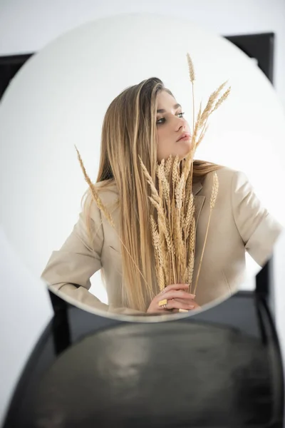 Reflection of young woman looking away while holding wheat with blurred chair on background — Stock Photo